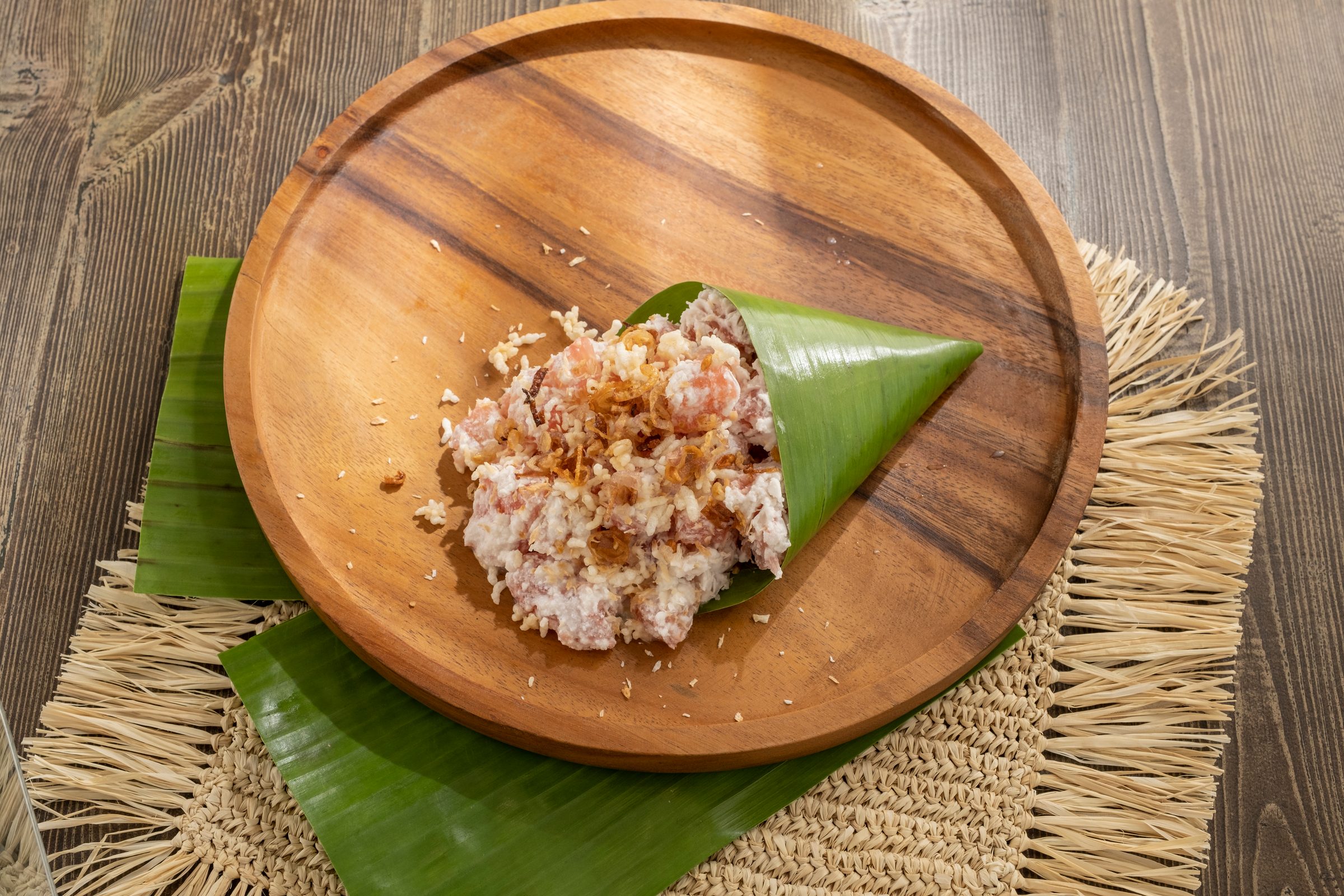 Pomelo salad with toasted coconut and fried shallots in a banana-leaf cone on a round wooden plate over banana leaves